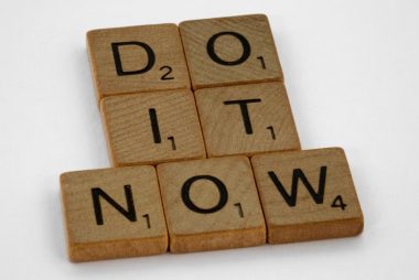 Wooden scrabble tiles forming 'DO IT NOW' on a minimal white backdrop. Inspiring concept.